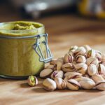 A jar of creamy pistachio butter with fresh pistachios around it.