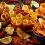 A colorful assortment of spicy chips with chili peppers and lime on a rustic background.