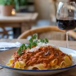 Freshly made pappardelle pasta with wild boar ragù, garnished with parsley and Parmesan, served on a rustic wooden table