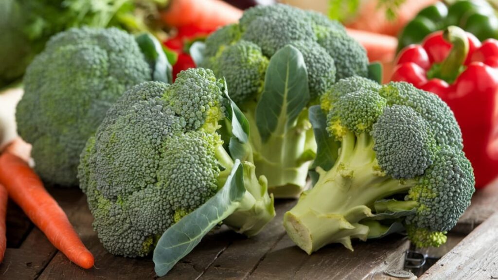 Fresh broccoli heads on a rustic wooden table with other colorful vegetables, highlighting its freshness and nutritional appeal.