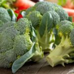 Fresh broccoli heads on a rustic wooden table with other colorful vegetables, highlighting its freshness and nutritional appeal.