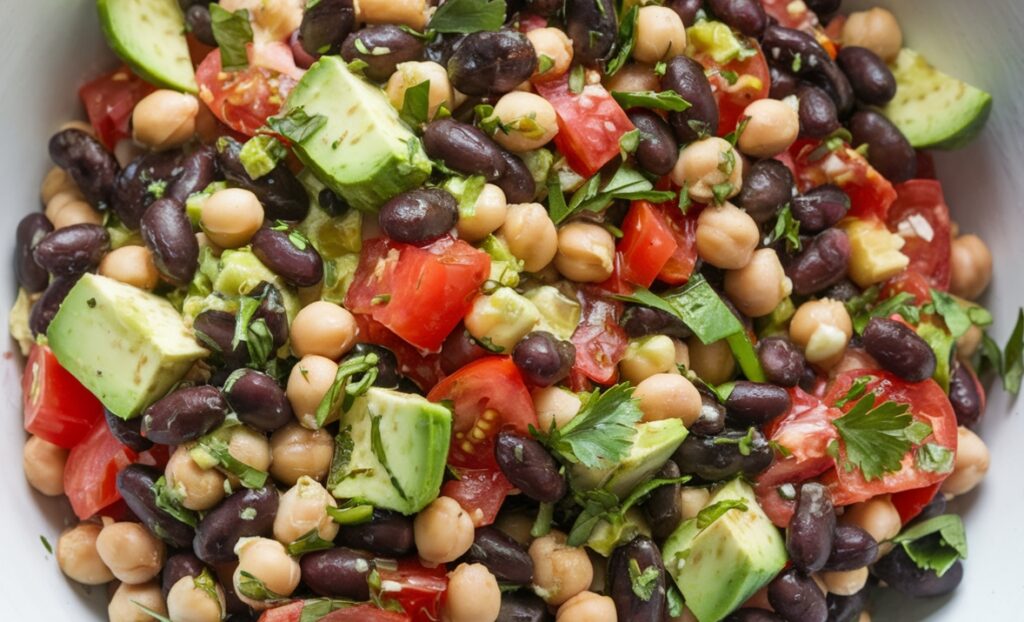 A colorful and healthy dense bean salad with black beans, chickpeas, tomatoes, cucumbers, and avocado.