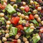 A colorful and healthy dense bean salad with black beans, chickpeas, tomatoes, cucumbers, and avocado.