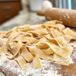 Wide pappardelle pasta with bolognese sauce and fresh basil on a rustic table